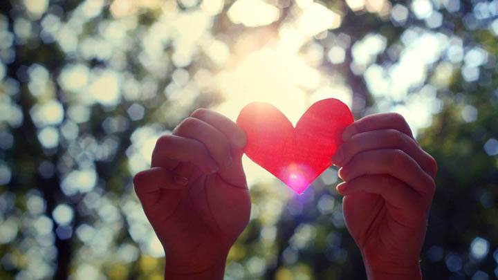 Two Hands Holding A Pink Paper Heart
